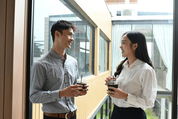 A man and a woman are standing next to each other, smiling and holding cups of coffee. They seem to be enjoying each other's company and having a pleasant conversation
