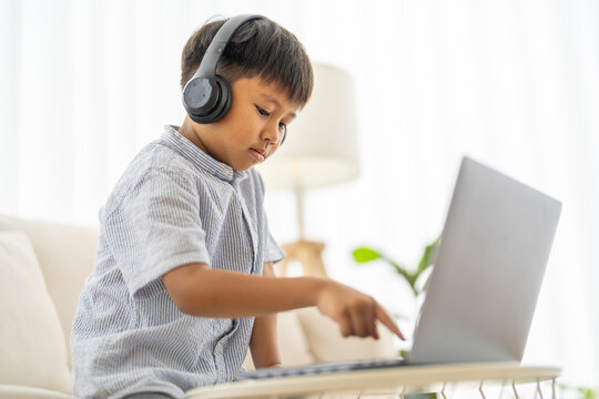 Asian boy using laptop with headphones course online learning, distance education for kids, e-learning at home, child studying digital technology, interactive education platform, remote class tutorial - Powered by Adobe