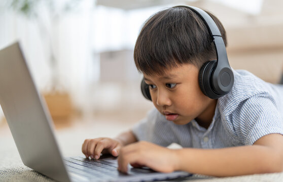 Asian boy using laptop with headphones course online learning, distance education for kids, e-learning at home, child studying digital technology, interactive education platform, remote class tutorial