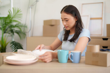 Adult Asian woman carefully packs dishes new home apartment relocation moving day household...
