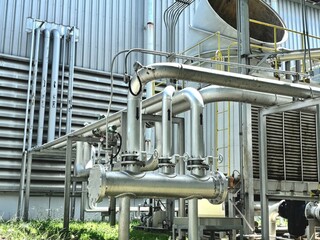 A complex network of industrial pipes and cooling units outside a factory or power plant. The shiny...