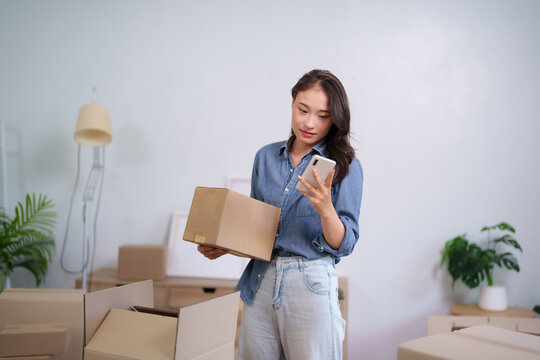 Asian adult woman busy packing moving boxes checking smartphone for shipping details new home relocation organization ecommerce delivery business management