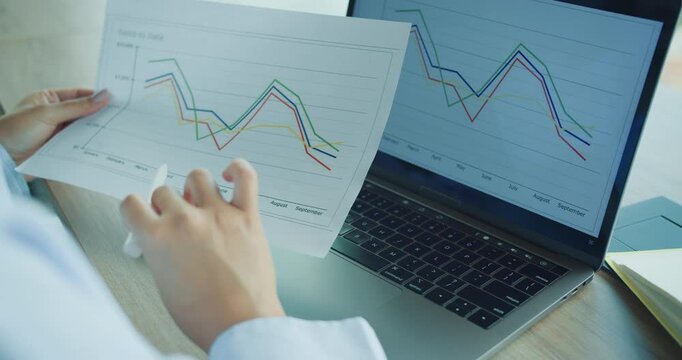 A professional diligently analyzing data trends on paper and a laptop in order to derive valuable insights