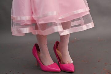 Close-up of girls feet in large pink shoes on gray studio floor. Child wears oversized heels,...