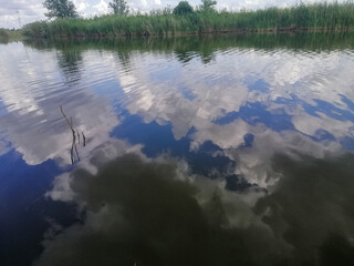 Summer rural landscape with calm river, clear sky and floating clouds. Nature appears relaxed and...