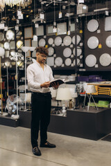 Man Browsing Catalog in a Lighting Store Showroom with Modern Fixtures Displayed