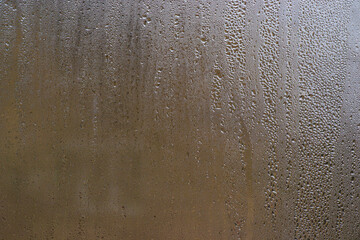 Tiny water droplets blanket fogged glass. some droplets already beginning to slide downward. wet glass of apartment window created an abstract background with natural pattern due to high humidity.