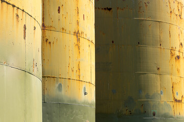 Close-up abstract view of cylindrical silos with rusted sections in green and yellow colors