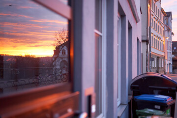 Reflection in the window. Sunrise in the city. House facade with garbage can.