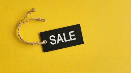 Bold black sale tag with twine against vibrant yellow background announces big savings event