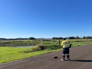Road worker brushing asphalt on sealed road in rural area