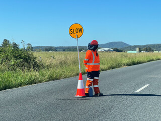 Road worker stand beside a slow down traffic sign