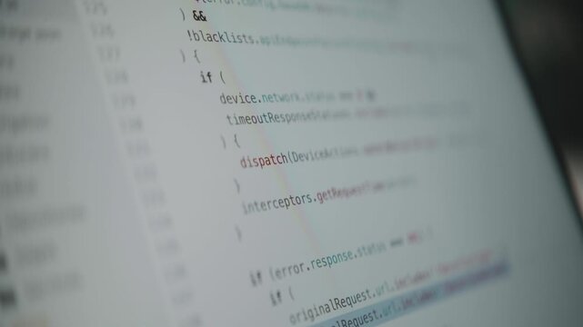 A close-up shot of a computer screen with lines of source code scrolling by quickly. A concept for programming, hacking, data streams, cyberspace, and modern technology