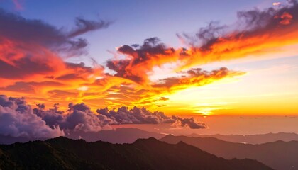 Fiery sunset over mountain ranges, clouds ablaze with orange and purple hues