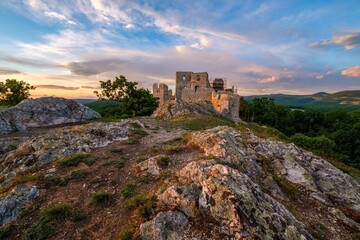 Obraz premium Medieval building illuminated by the setting sun and blue sky with clouds. Ruins of Hrusov Castle, an ancient feudal castle located in West Slovakia near city Nitra. History old Hungary and Austria.