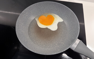 Heart-shaped egg yolk in a non-stick frying pan on a stovetop, creating a cute and romantic breakfast moment. Perfect for cooking, love, or food-themed content.