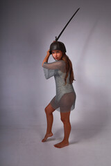 Slender young barefoot woman in chainmail and original medieval Asian helmet holding sword and...