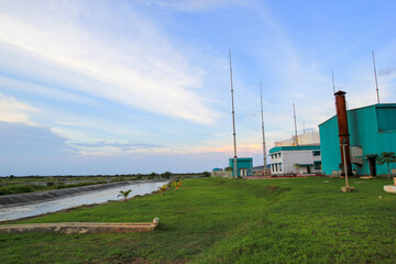 Industrial facility by water with green field and blue sky