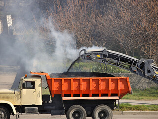 Loading crushed hot asphalt onto a truck. Asphalt removal using heavy machinery. Construction and repair of the road. Modern technology of laying a highway with a solid surface. People work
