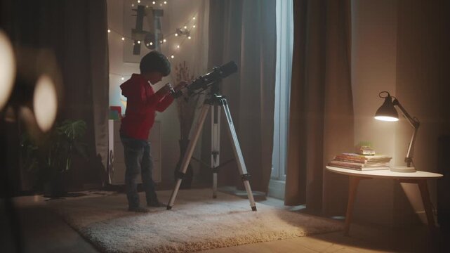 A curious young boy uses a telescope in his room at night to explore the stars. A concept of childhood dreams, science education, an astronomy hobby, and inspiring wonder.