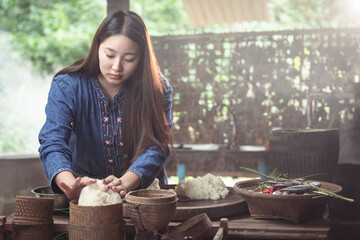 A young woman uses her hands to arrange and pack freshly made sticky rice into a traditional Kratip...