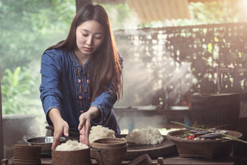 In her rustic kitchen, a woman portions sticky rice into baskets, with the rest of the meal ready...