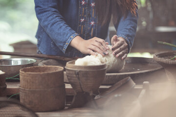 A detailed close-up shows hands carefully forming sticky rice in a woven basket. This image celebrates the tactile craftsmanship and heritage behind simple, everyday Thai food.
