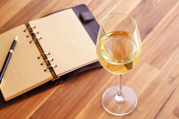 Glass of white wine and open notebook on table
