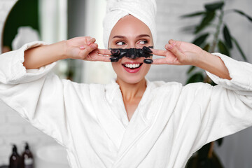 Woman enjoying a beauty treatment at home while smiling and wearing a towel on her head