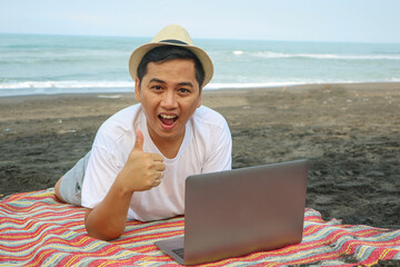 Young tourist man wear beach shirt hat lie on deckchair hold use work on laptop pc computer show...