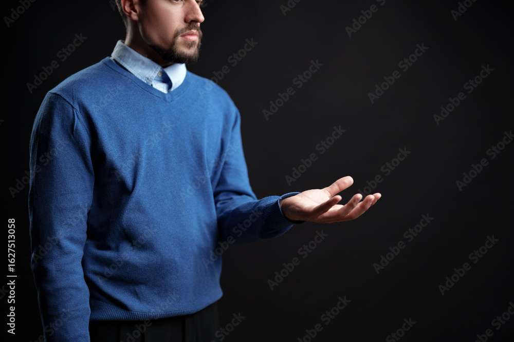 Poster man in blue sweater with open hand gestures in a studio setting during evening