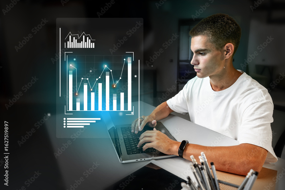 Poster young man analyzes data on a laptop while visualizing graphs in a modern workspace during late eveni
