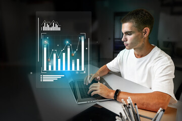 Young man analyzes data on a laptop while visualizing graphs in a modern workspace during late evening hours