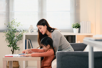 Mother assisting her daughter working on school assignments and creative tasks at home