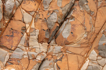 A vibrant, close-up view of a rugged seaside rockface, showcasing its rich orange hues and...
