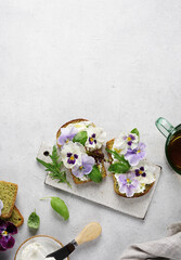 Breakfast cream cheese toast with pansies flowers on plate, on white marble background. top view, copy space