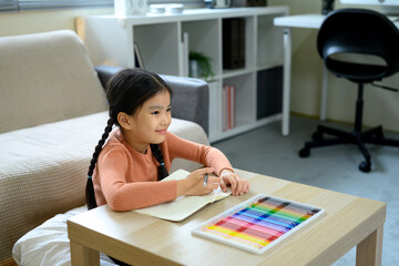 Happy child doing homework or art project sitting at wooden table with vibrant coloring pens