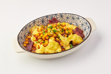 Baked dish featuring melted cheese, sweet corn, and crispy bacon, garnished with chopped green onions, served in patterned ceramic bowl on white background