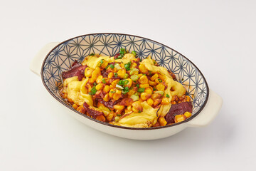 Baked dish featuring melted cheese, sweet corn, and diced vegetables, garnished with green onions, served patterned ceramic dish. vibrant colors and creamy texture evoke comforting and appetizing