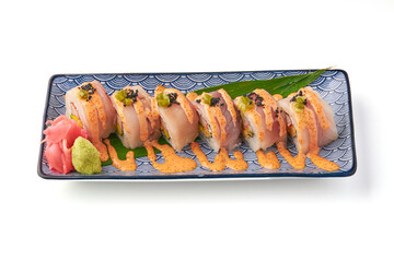 Sushi roll topped with fresh fish slices, spicy mayo, and garnished with wasabi, pickled ginger, and caviar on decorative plate. presentation is elegant and appetizing
