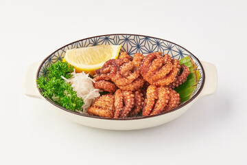 Crispy fried octopus tentacles served in decorative bowl with fresh parsley, shredded radish, lemon wedge, and banana leaf garnish, offering vibrant and appetizing presentation
