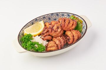 Crispy fried octopus tentacles served in decorative bowl with fresh parsley, shredded radish, lemon wedge, and green garnish, offering delightful and savory presentation