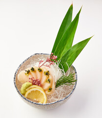 Freshly sliced sashimi scallops served on shredded radish with lemon, wasabi, and garnished with herbs and edible flowers in decorative bowl