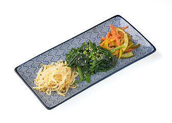 Beautifully arranged plate of Korean vegetable side dishes, including seasoned spinach, pickled radish, and stir fried vegetables, garnished with sesame seeds, served patterned rectangular plate