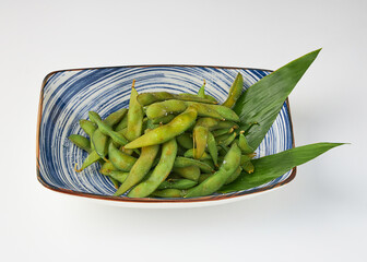 Steamed edamame beans served in blue and white ceramic bowl with green leaves, creating fresh and healthy presentation