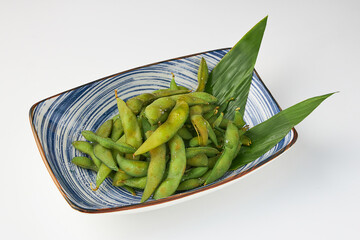 Steamed edamame beans served in blue ceramic bowl with green leaves, offering healthy and nutritious snack option
