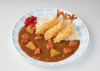 Crispy fried shrimp served on plate of Japanese curry with rice, garnished with pickled vegetables. dish features rich, flavorful curry sauce with chunks of carrots and potatoes