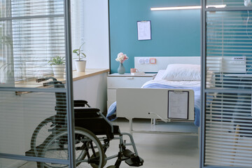 Empty hospital room featuring wheelchair with disability positioned near bed, medical equipment...