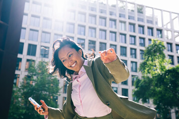 Smiling businesswoman outdoors in city holding phone showing joy