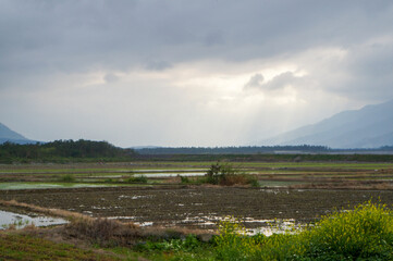Vast Rural Landscape with Flooded Fields and Distant Mountains under a Dramatic Cloudy Sky.